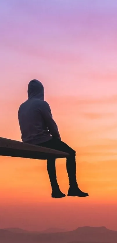 Silhouette figure sits against an orange sunset sky.