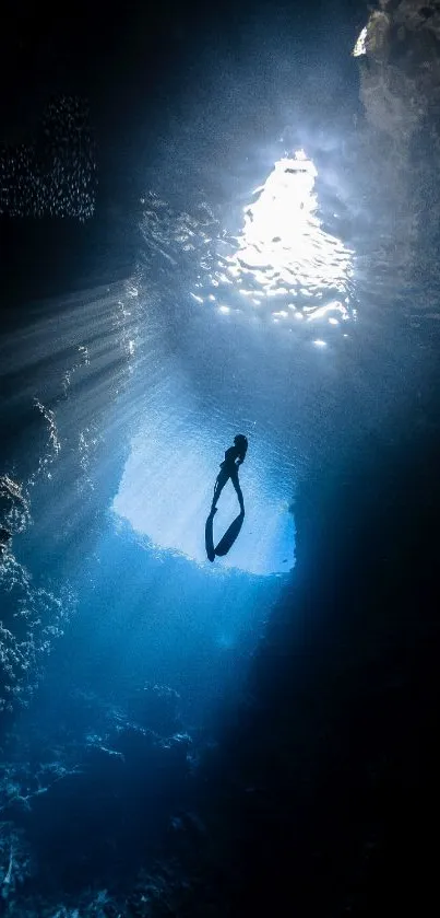 Silhouette diver exploring a blue underwater cave with light rays.