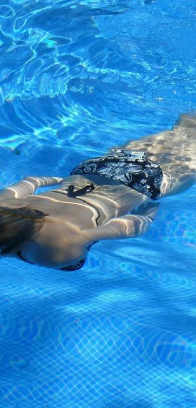 Woman swimming underwater in a sunlit blue pool, creating a serene and peaceful scene.