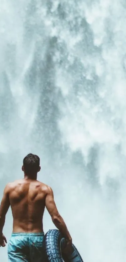 Man with tire facing majestic waterfall.