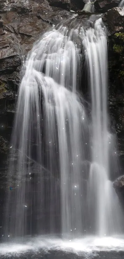 Tranquil waterfall cascading down rocky cliffs surrounded by lush greenery.