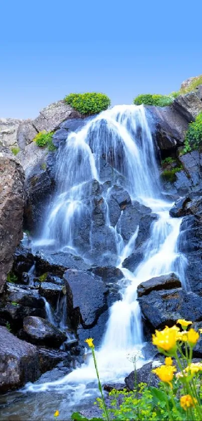 Serene waterfall over rocks with blue sky and flowers.