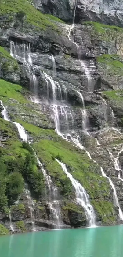 Cascading waterfalls over a lush green hillside with serene turquoise water below.