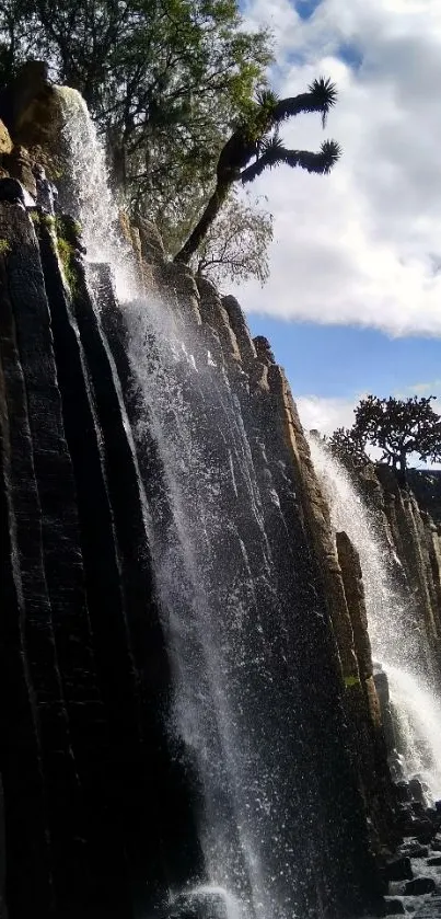 Serene waterfall with blue sky and rock formations, perfect for phone wallpaper.