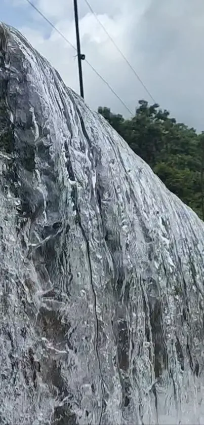 Serene waterfall cascading over rocks with lush green surroundings and cloudy sky.