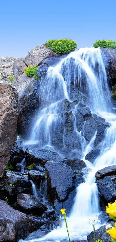 Beautiful waterfall surrounded by rocks and greenery with a clear blue sky.