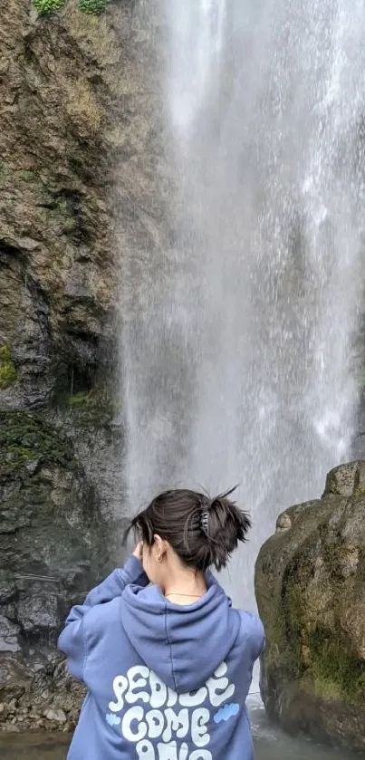 A person stands before a cascading waterfall.