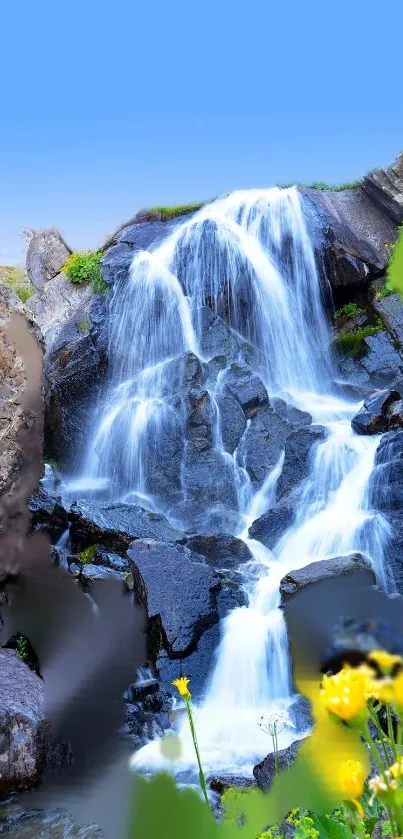 Beautiful waterfall cascading over rocks with blue sky and yellow flowers.