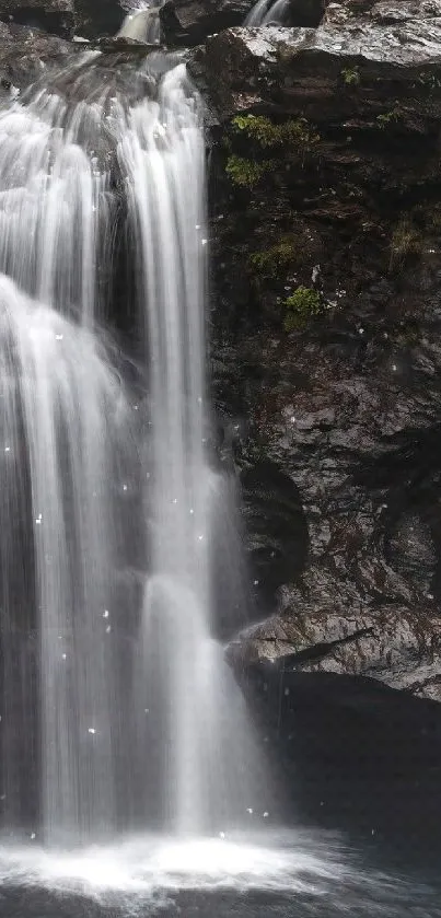 Serene waterfall with dark rocks and lush green foliage.