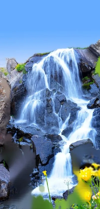 A serene waterfall with vibrant yellow flowers and lush greenery under a clear sky.