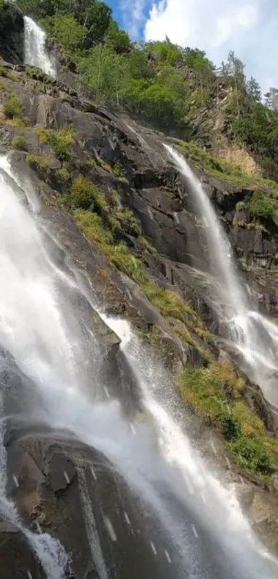 Waterfall cascading down rocky cliffs in lush green landscape.