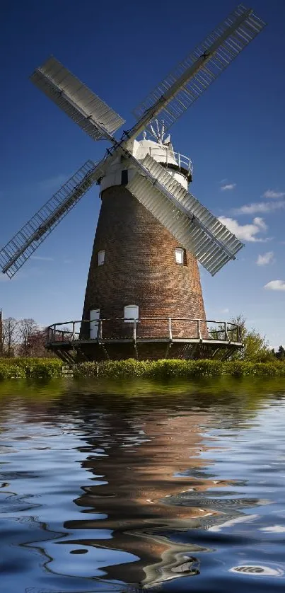 Windmill reflecting on tranquil lake under blue sky.