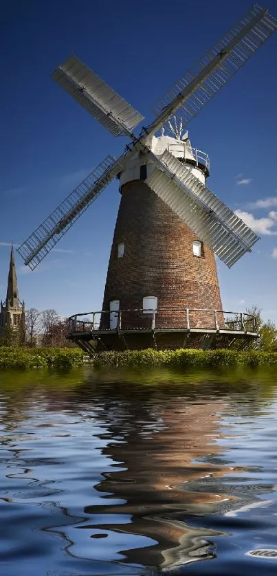 Windmill reflection on water with clear blue sky.