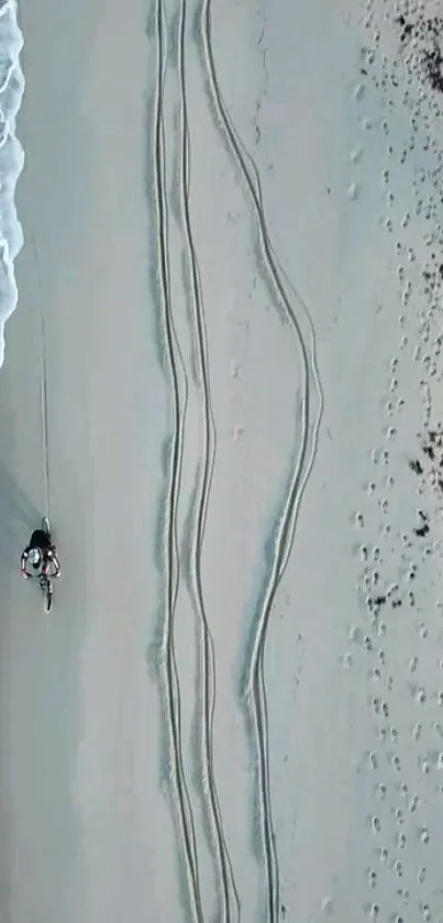 Aerial view of serene beach with waves and bike tracks on sand.