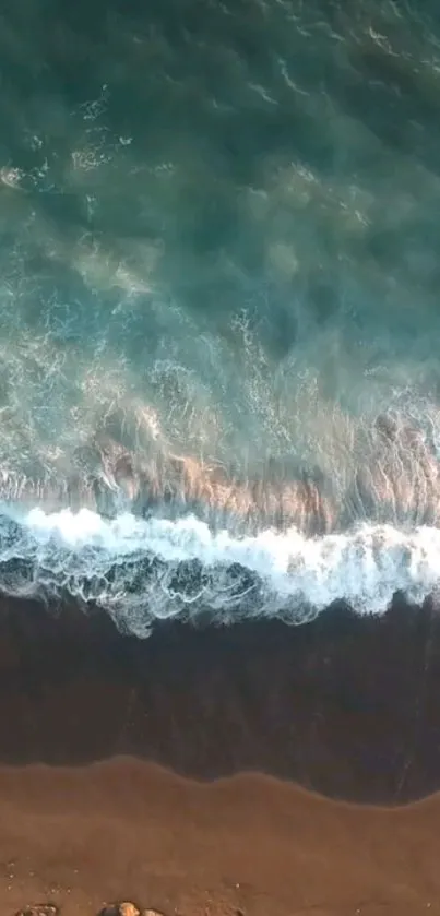 Aerial view of teal ocean waves crashing on a sandy beach.