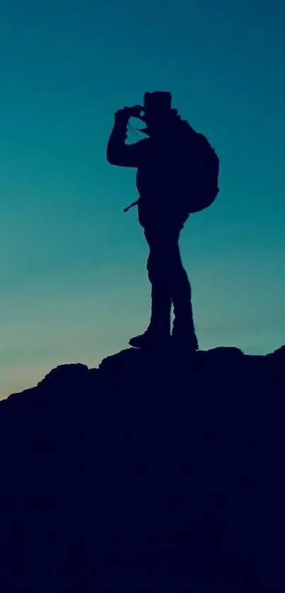 Silhouette of adventurer at dusk on a rocky peak with teal sky.