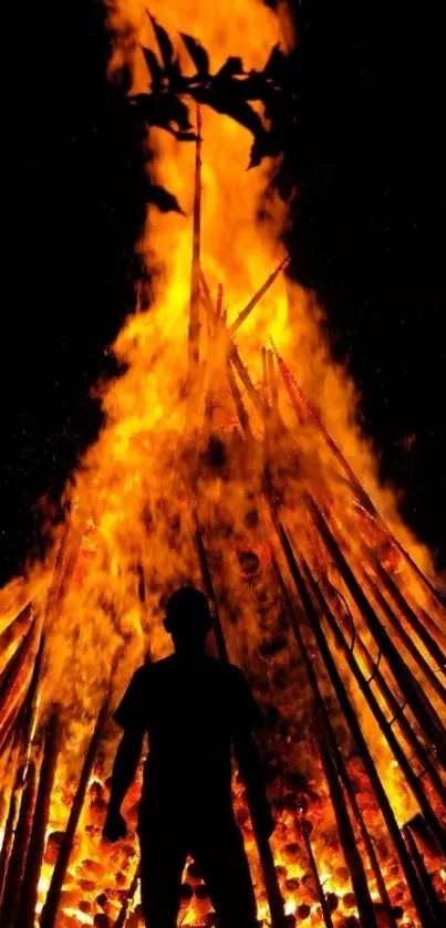 Silhouette standing against a towering bonfire with bright orange flames.