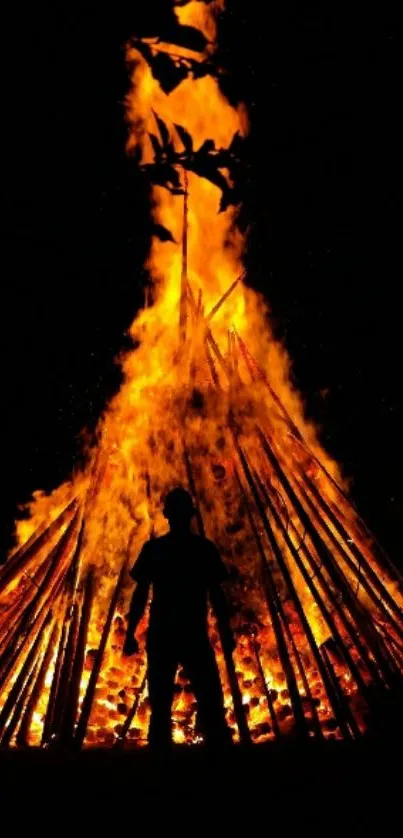 Silhouette standing before a large bonfire glowing brightly.