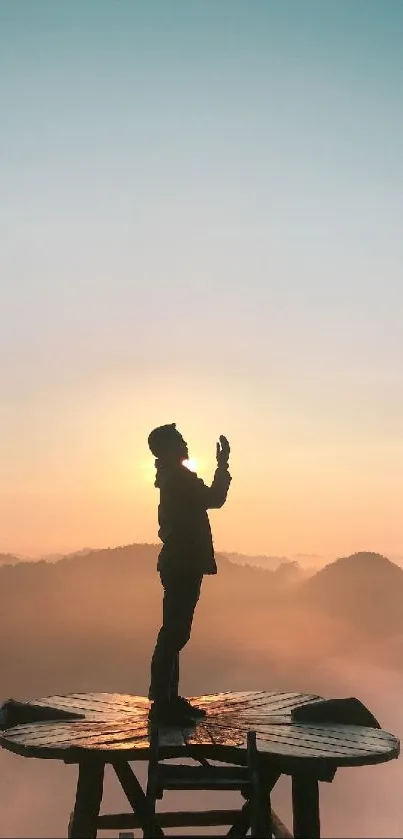 Silhouette on platform against sunrise over mountains.