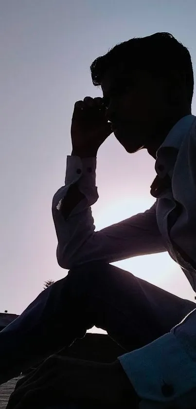 Silhouette of a person sitting at sunset against a gradient sky.