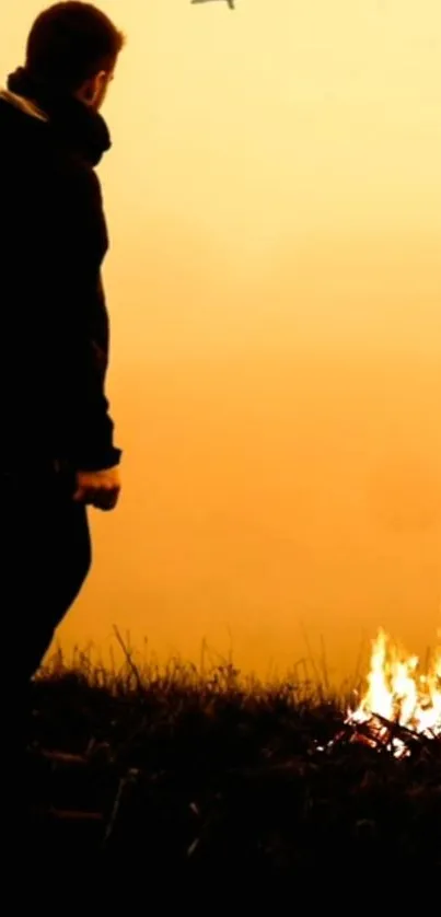 Silhouette of person by a fire during orange sunset.