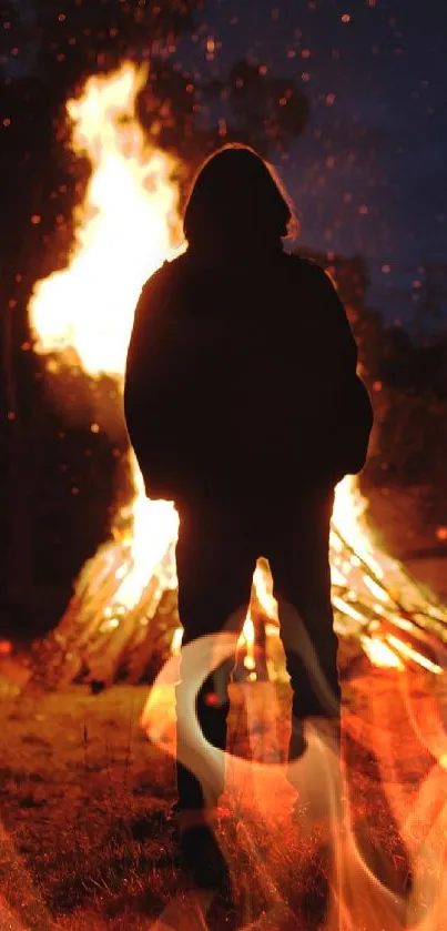 Silhouetted figure standing before a large bonfire at night.