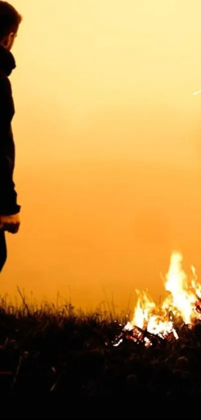 Silhouette of person beside campfire against orange sky.