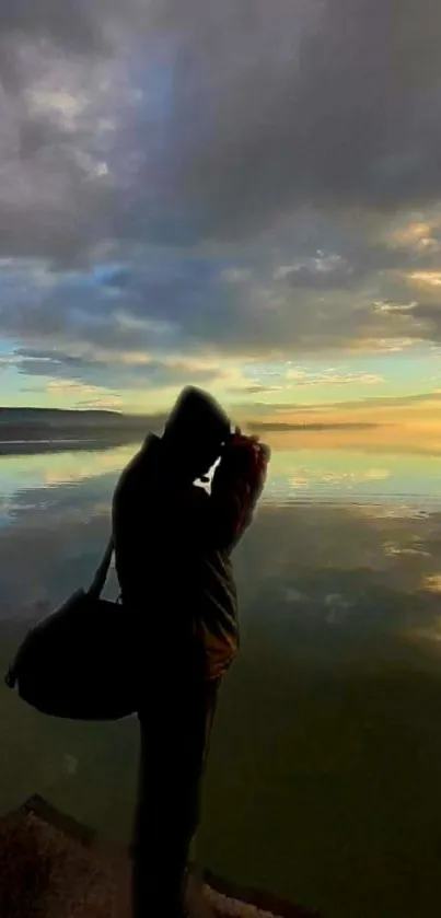 Silhouette of a person by a tranquil, reflective lake at sunset.