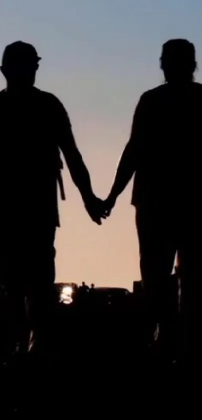 Silhouette of couple holding hands at sunset.