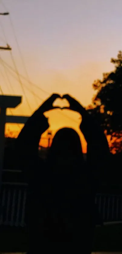 Silhouette of a person making a heart shape against a sunset background.