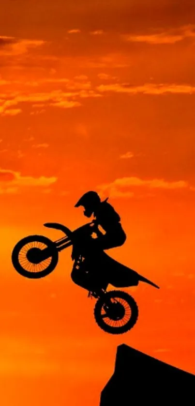 Motocross biker silhouetted against an orange sunset sky.