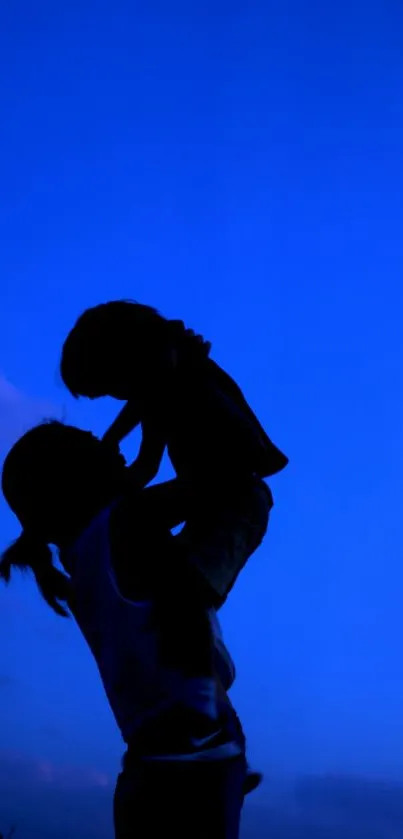 Silhouette of a parent lifting a child against a cobalt blue sky backdrop.