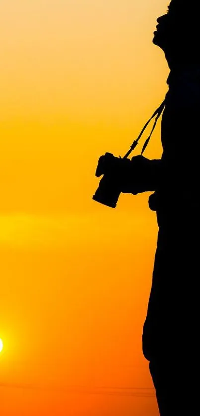 Silhouette of photographer with camera against a vibrant orange sunset.