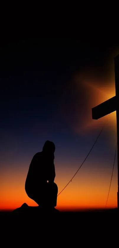 Silhouette of a person kneeling beside a cross during a beautiful sunset.