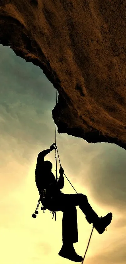 Silhouette of rock climber against a cliff and sunset sky.