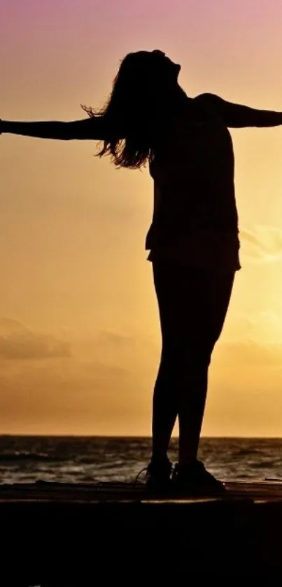 Silhouette of a person with outstretched arms against a vibrant sunset over the ocean.