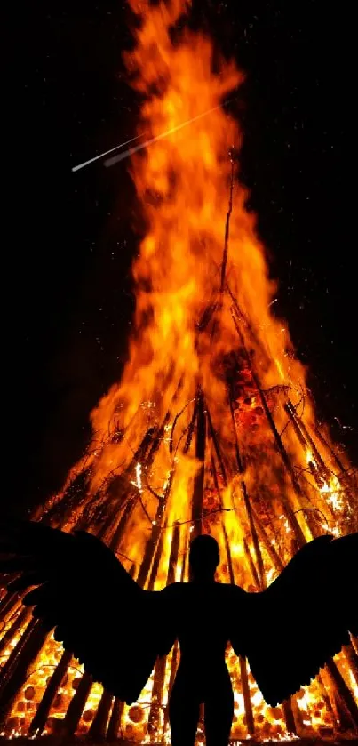 Silhouette with wings in front of large orange bonfire at night.