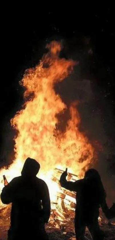 Silhouettes against a vibrant bonfire at night, casting dramatic shadows.