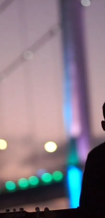 Silhouette of a man with guitar by colorful lit bridge at sunset.