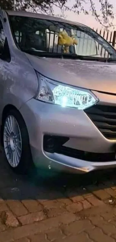 Silver car parked on a brick road in an evening urban setting.