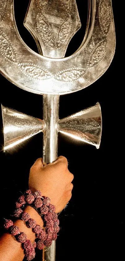 Handcrafted silver trident held against a black background, artistic and symbolic.