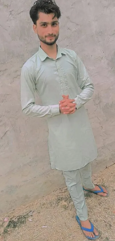 Man in traditional attire standing outdoors against a light background.