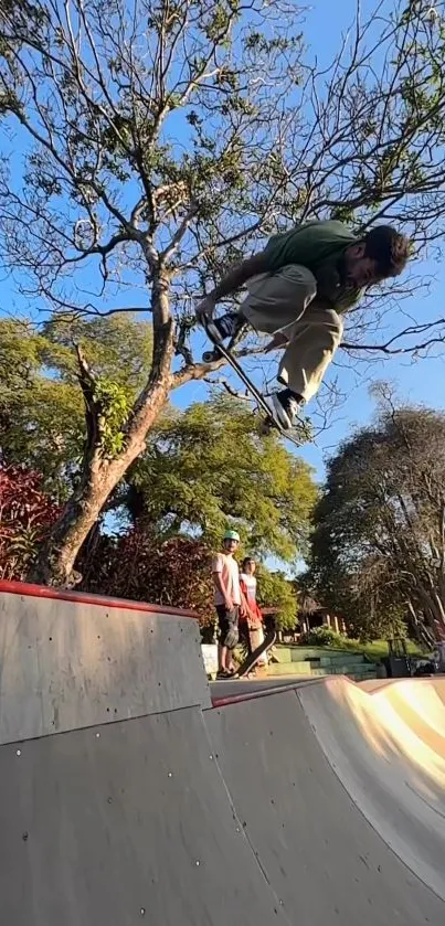 Skateboarder jumps high near trees under blue sky in skate park.