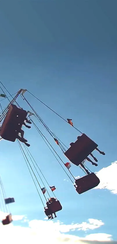 Carnival ride swings against a blue sky with clouds. Silhouetted chairs in motion.