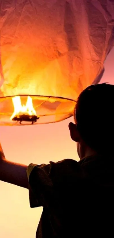 Child releasing an orange glowing lantern at sunset.