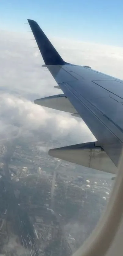 Airplane wing view from window above clouds and cityscape.