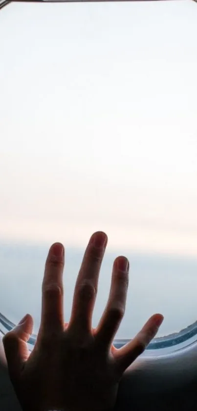 Hand reaching out to a bright sky through an airplane window, capturing travel vibes.