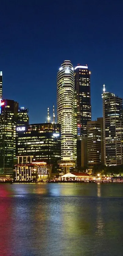 A vibrant city skyline at night with reflections on calm waters under a dark blue sky.