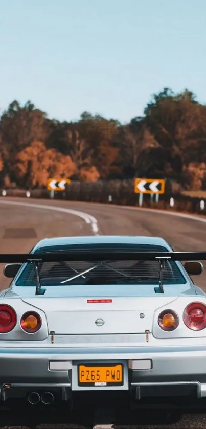 Silver Nissan Skyline on a scenic winding road with autumn trees.