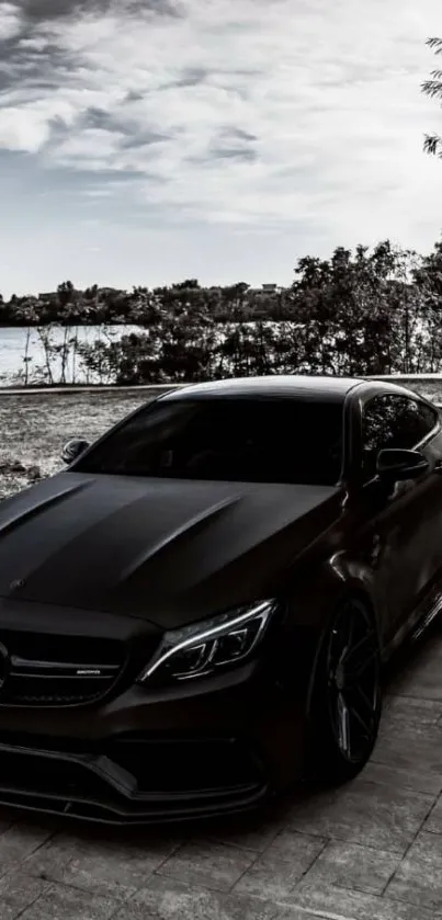 Black luxury car by lakeside with clouds.